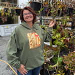 Person wearing a green hoodie with a floral design, standing in a garden setting.