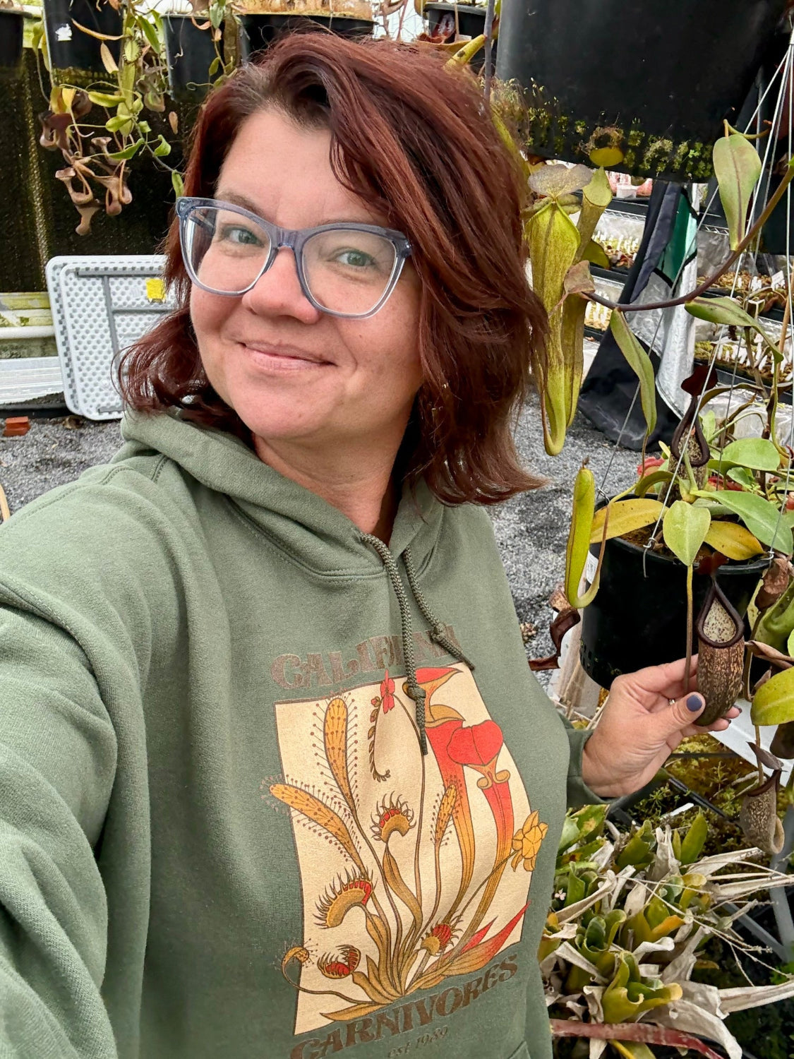 Person wearing a green hoodie with a plant design, standing among plants.
