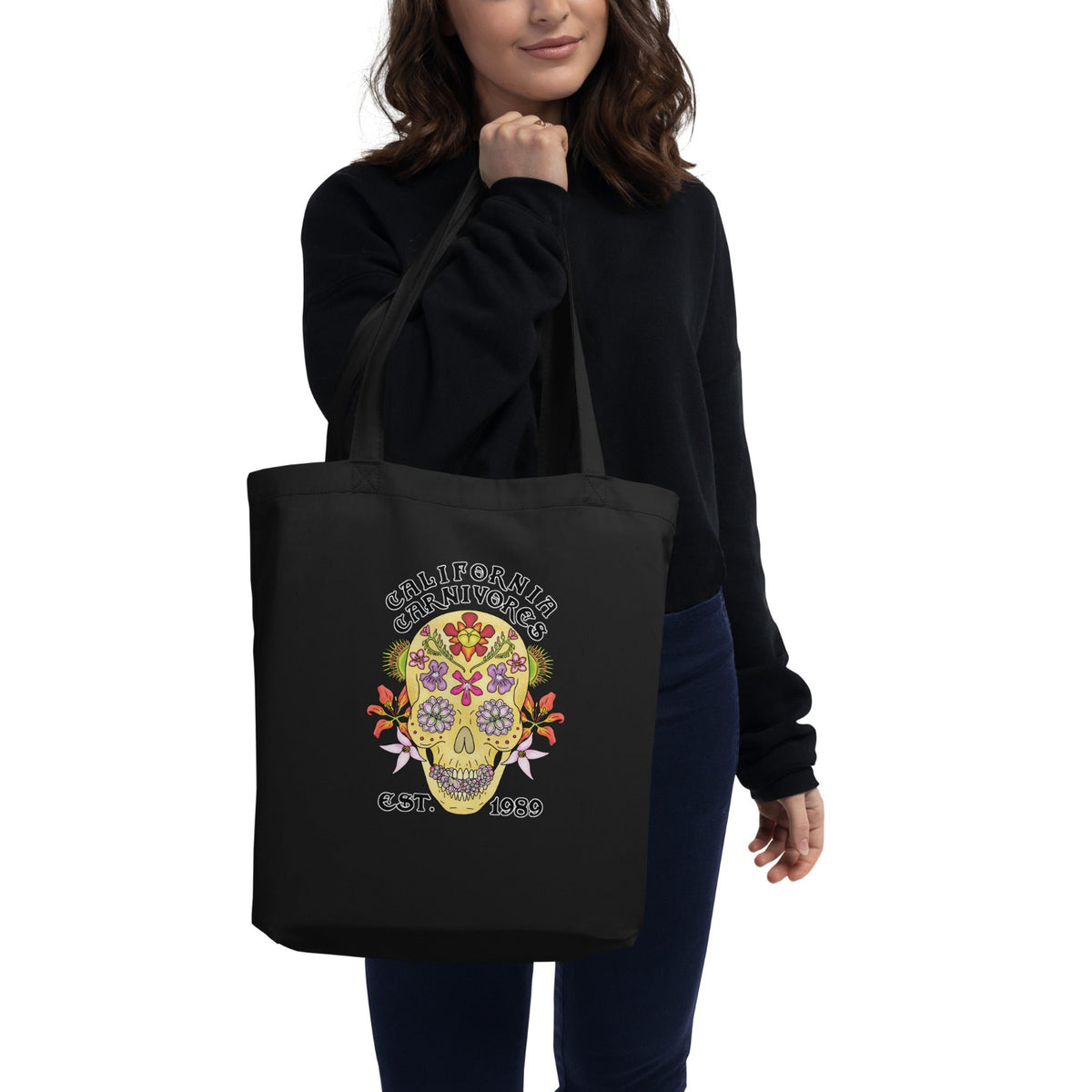 Person holding a black tote bag with a colorful skull design and text.