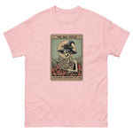Pink t-shirt with a graphic of a skeleton in a witch hat and cape, holding a book, on a white background.