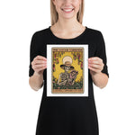 Person holding a print of 'The Savage Gardener' with a skeleton wearing a hat and holding a plant.