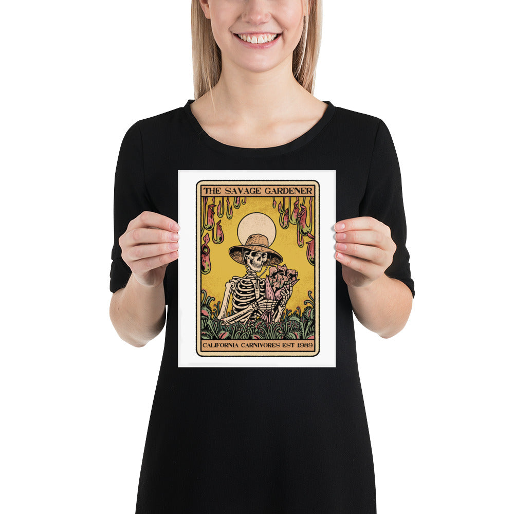 Person holding a print of 'The Savage Gardener' with a skeleton wearing a hat and holding a plant.