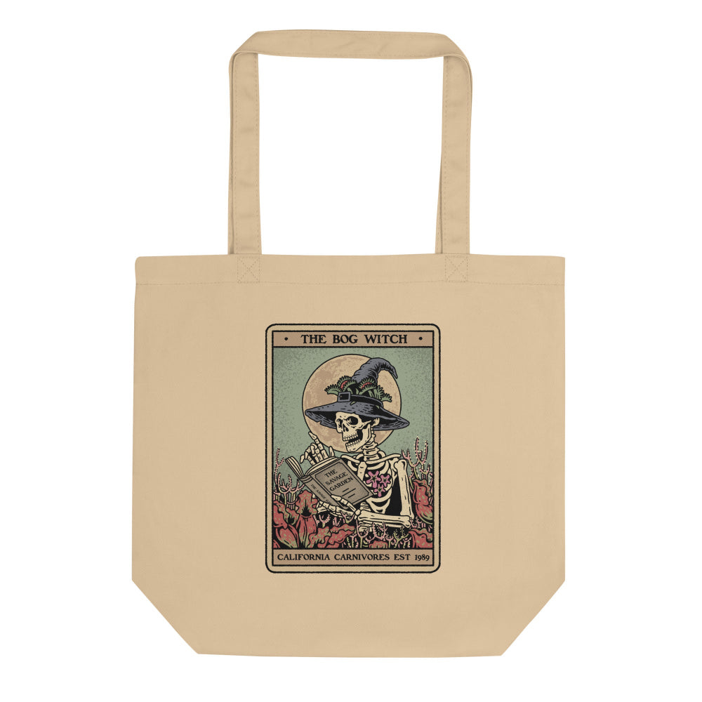 Beige tote bag with a graphic of a skeleton wearing a witch hat and holding a book, labeled 'The Bog Witch'.