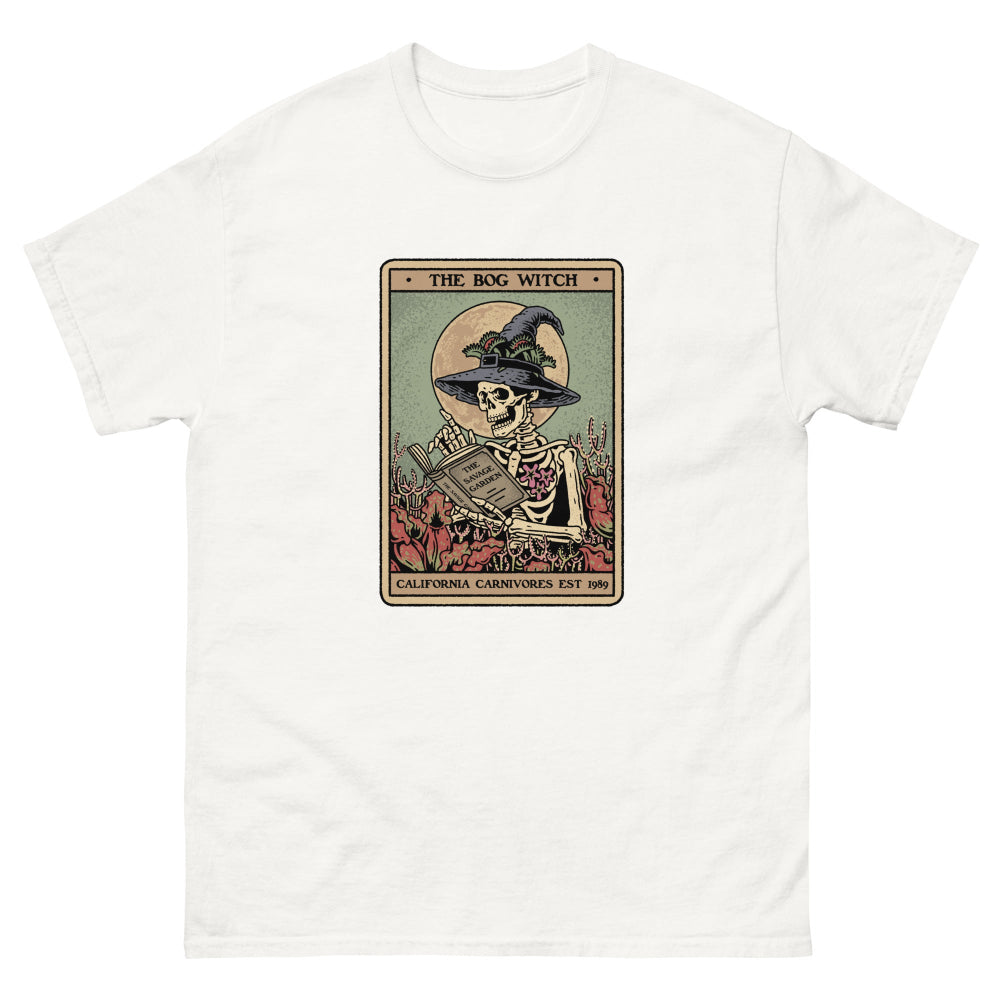 White t-shirt with a graphic of a skeleton in a witch hat and cape, sitting on a card with text 'The Bog Witch' on a white background.