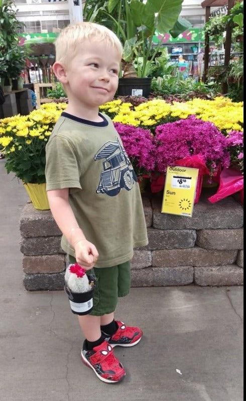 A small child holds a cactus in a plant nursery